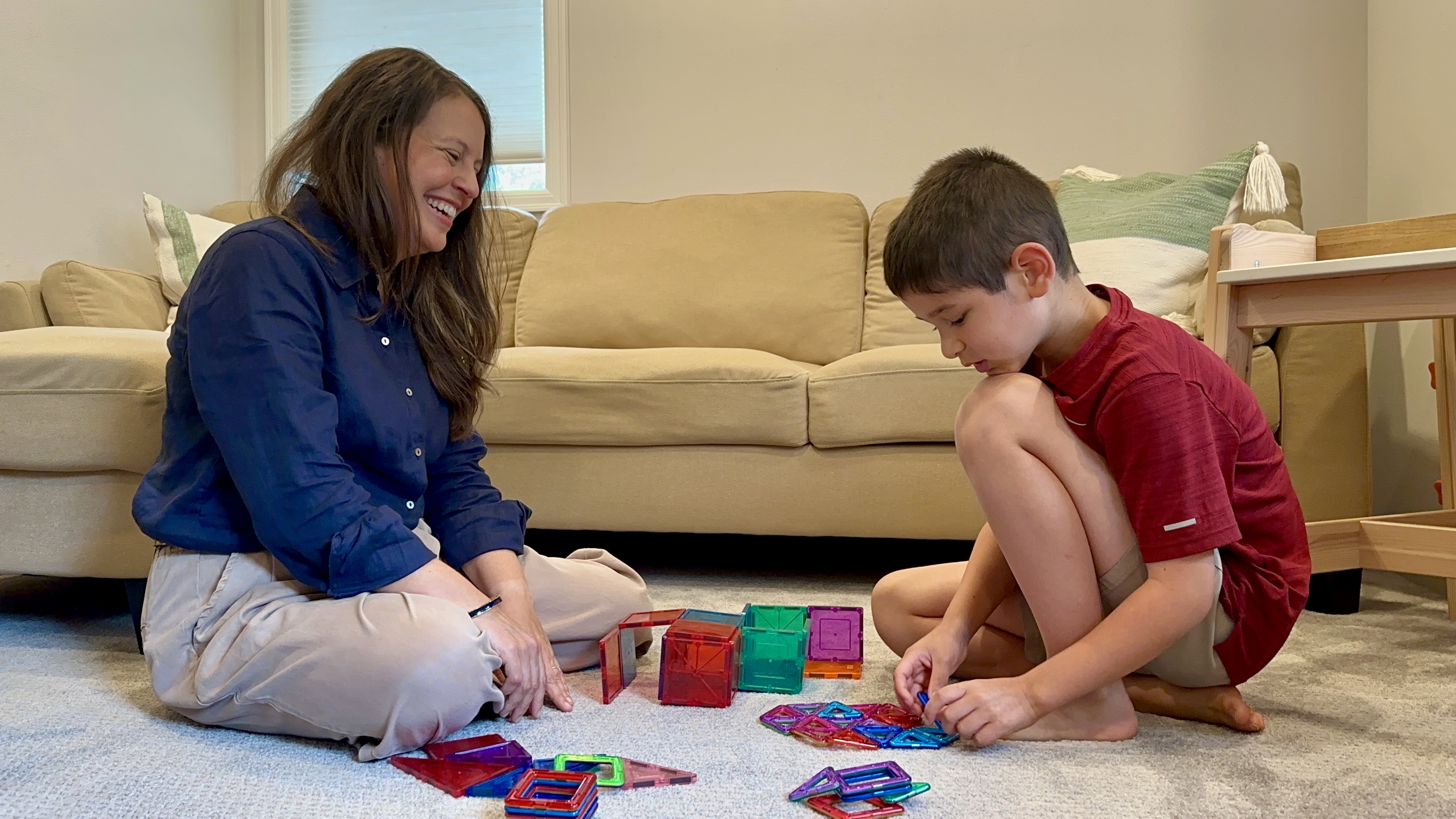 Yvonne Ontiveros, LICSW, playing on the floor with a child using colorful magnetic tiles — a warm, relaxed session capturing the spirit of child-centered play therapy